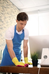 Young man in apron and gloves cleaning office