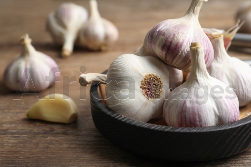 Fresh organic garlic in bowl on wooden table, closeup