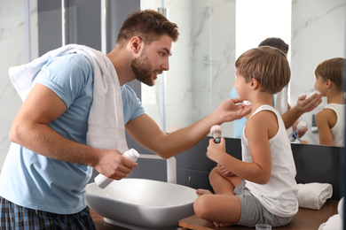 Dad applying shaving foam onto son's face in bathroom
