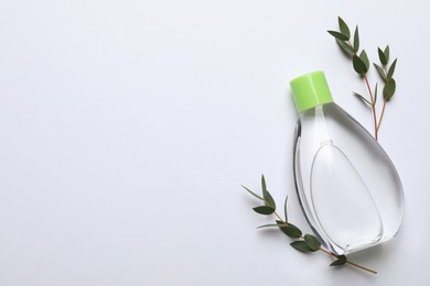 Bottle of baby oil and leaves on white background, flat lay. Space for text
