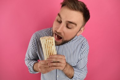 Photo of Young man eating delicious shawarma on pink background