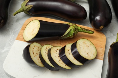 Photo of Cut and whole raw ripe eggplants on grey table, closeup