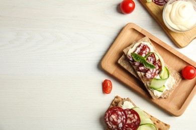 Photo of Fresh rye crispbreads with salami, cream cheese and cucumber on white wooden table, flat lay. Space for text