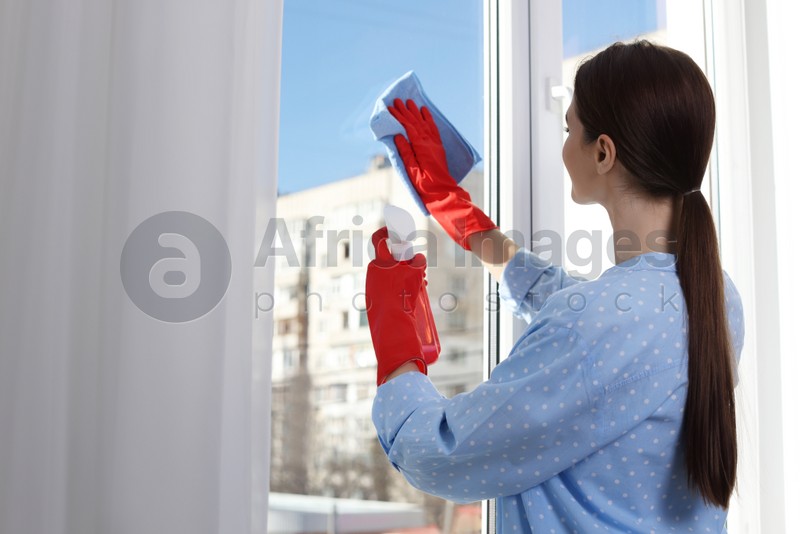 Photo of Young woman cleaning window glass with rag and detergent at home, back view. Space for text