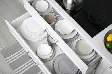 Photo of Open drawers with different plates and bowls in kitchen, above view