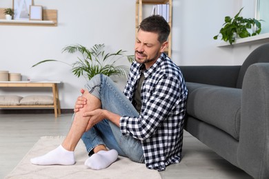 Man rubbing sore leg near sofa at home
