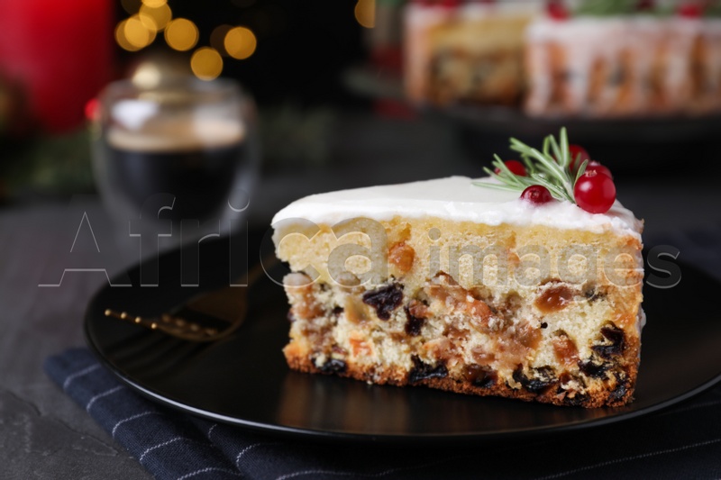 Photo of Slice of traditional Christmas cake decorated with rosemary and cranberries on black table, closeup