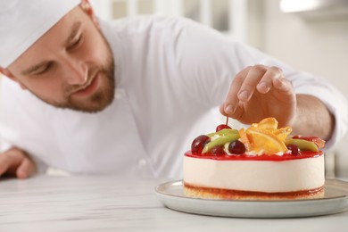 Happy professional confectioner decorating delicious cake at table in kitchen