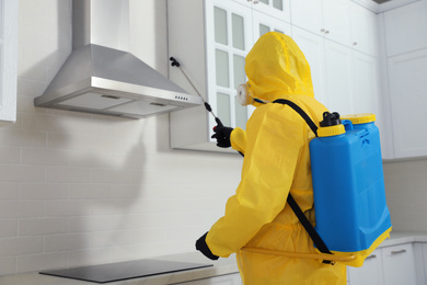 Pest control worker in protective suit spraying insecticide on furniture indoors. Space for text