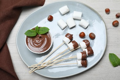 Tasty marshmallows dipped into chocolate on white wooden table, top view