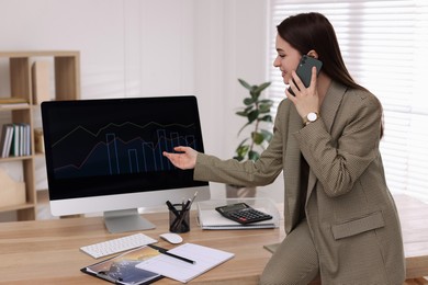 Businesswoman talking on phone while working with computer in office. Forex trading