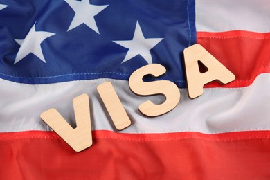 Word Visa made of wooden letters on American flag, flat lay. Immigration to USA