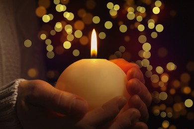 Closeup view of woman holding burning candle in darkness, bokeh effect. Christmas Eve