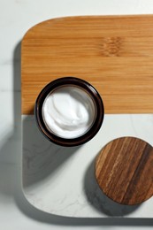 Board with open jar of cosmetic cream on white table, top view