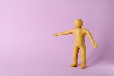 Human figure with arms wide open made of yellow plasticine on violet background. Space for text