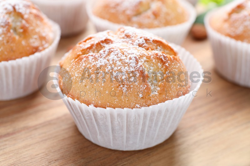 Photo of Tasty muffins powdered with sugar on wooden board, closeup