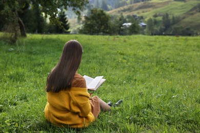 Young woman reading book on green meadow, back view