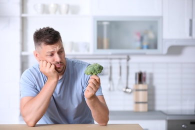 Portrait of unhappy man looking at broccoli in kitchen