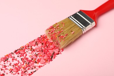 Photo of Brush painting with red sprinkles on pink background, closeup. Creative concept