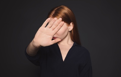 Young woman making stop gesture against dark background, focus on hand