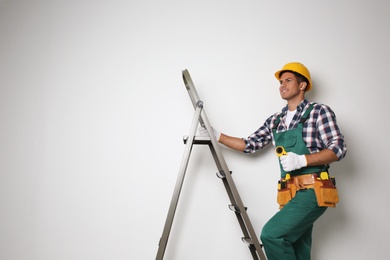 Professional builder climbing up metal ladder on light background. Space for text