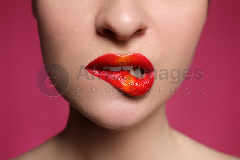 Young woman with beautiful makeup biting lip on pink background, closeup