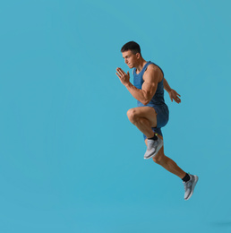 Athletic young man running on turquoise background, side view