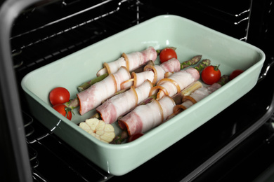 Uncooked bacon wrapped asparagus in baking dish on oven rack, closeup