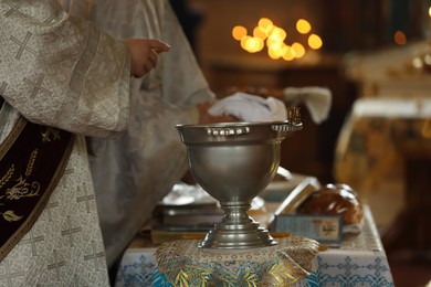 Priests preparing for baptism ceremony. Silver vessel with holy water on stand in church