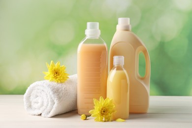 Photo of Bottles of laundry detergents, towel and beautiful flowers on white wooden table