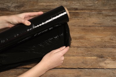 Photo of Woman unrolling black plastic stretch wrap on wooden background, closeup. Space for text