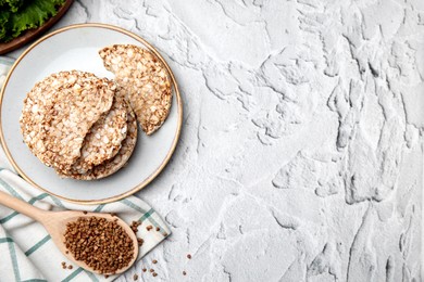Crunchy buckwheat cakes and spoon with cereal on white textured table, flat lay. Space for text