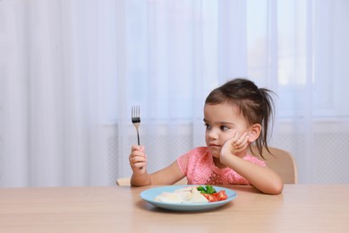 Cute little girl refusing to eat her breakfast at home, space for text