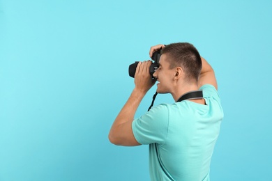 Photo of Young professional photographer taking picture on light blue background. Space for text