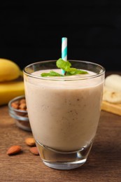 Glass with banana smoothie and mint on wooden table against black background