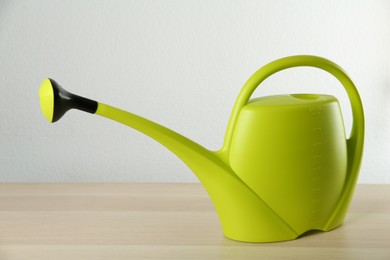 Photo of Green plastic watering can on wooden table against white background