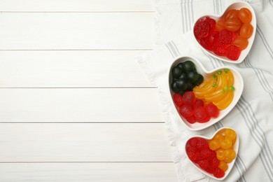 Delicious gummy fruit shaped candies on white wooden table, flat lay. Space for text