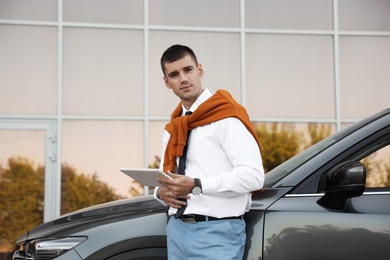 Attractive young man with tablet near luxury car outdoors