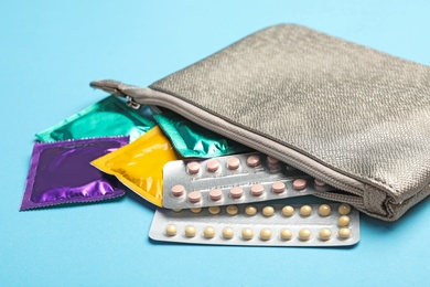Cosmetic bag with condoms and birth control pills on light blue background. Safe sex concept