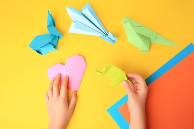 Photo of Origami art. Child holding paper figures on yellow background, closeup and top view
