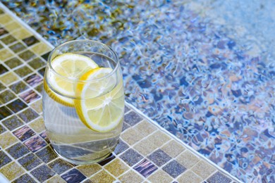 Photo of Refreshing water with lemon on edge of swimming pool, space for text