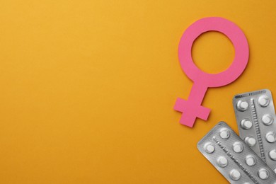 Female gender sign, blisters of pills and space for text on orange background, flat lay. Women's health concept