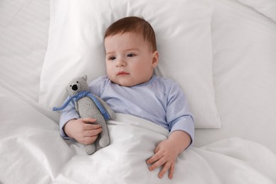 Photo of Cute little baby with toy lying in bed under soft blanket, top view