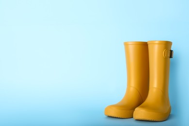 Pair of yellow rubber boots on light blue background. Space for text