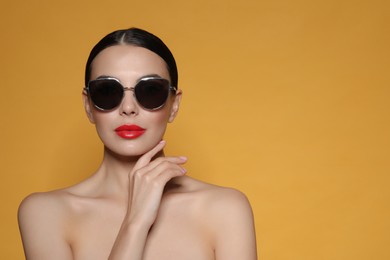 Attractive woman in fashionable sunglasses against orange background. Space for text