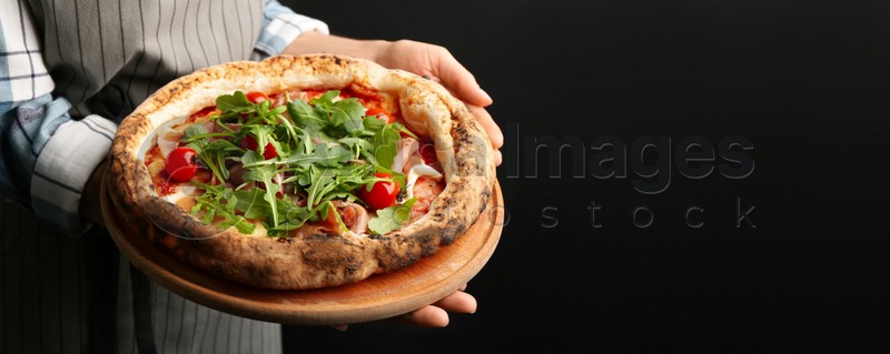 Woman holding tasty pizza with meat and arugula on black background, closeup view with space for text. Banner design