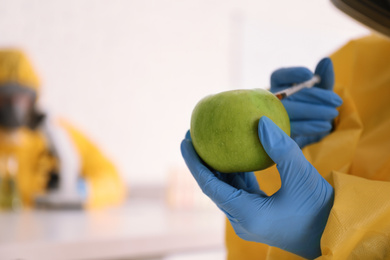 Scientist in chemical protective suit injecting apple at laboratory, closeup with space for text