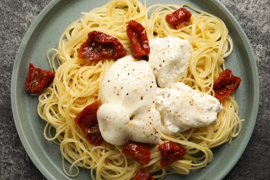 Delicious spaghetti with burrata cheese and sun dried tomatoes on grey table, top view