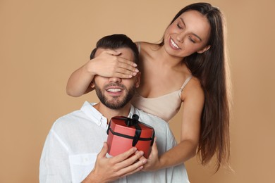 Woman presenting gift to her boyfriend on beige background