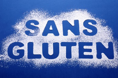 Phrase Gluten free written in French with flour on blue background, top view